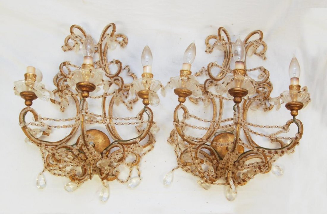 PAIR OF ANTIQUE CUT CRYSTAL WALL SCONCES: A pair of antique French cut crystal and gilded metal three arm sconces. Each heavily decorated with cut crystal prisms. Circa 19th century. Measures 20" height x 15" width (50.8cm x 38.1cm). Provenan
