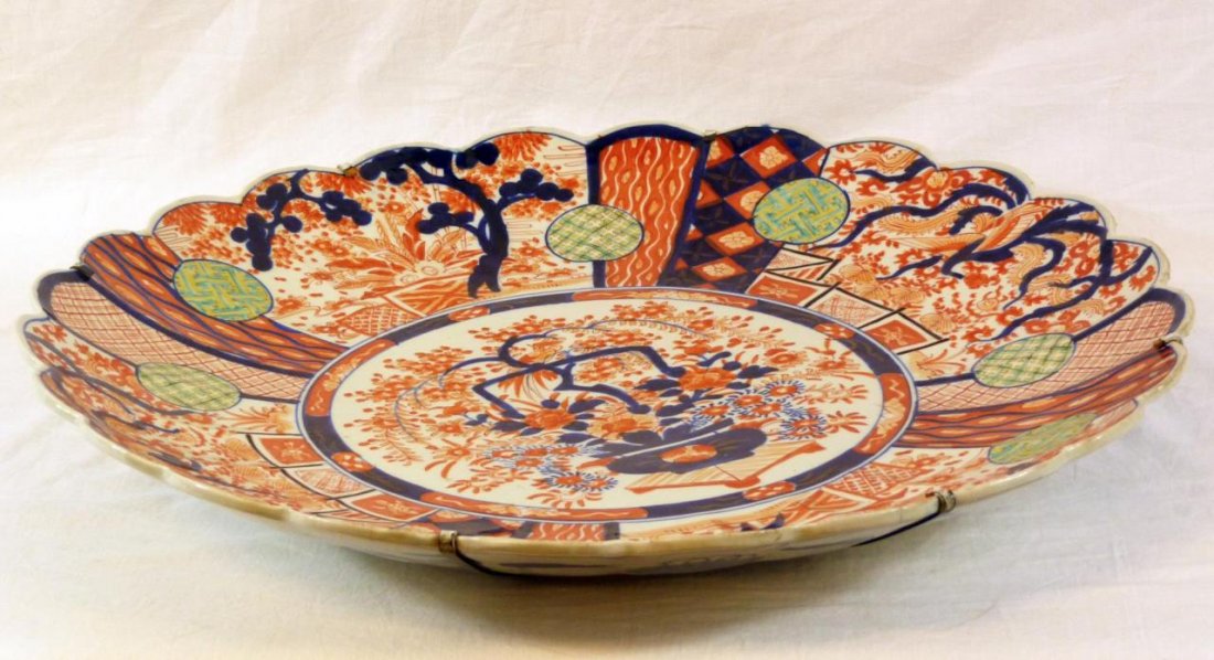 19th CENTURY JAPANESE IMARI SCALLOPED CHARGER: Antique Japanese hand painted red and white Imari scalloped charger depicting floral designs throughout with wucai medallions housing patterns. Urn with floral bouquet to center. Exterior having a blu