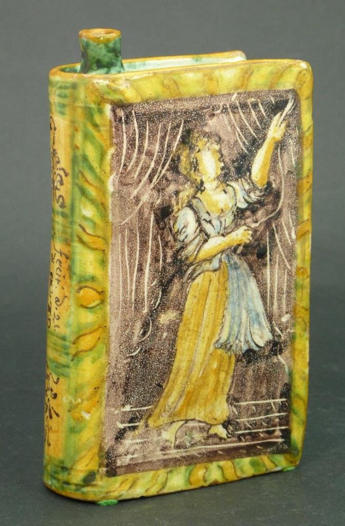 ENGLISH DELFT TIN GLAZED EARTHENWARE HAND WARMER: Late 18th century English Delftware tin glazed pottery hand warmer. Modeled in the form of a book with portrait of woman to front and back cover. Spine dated 1796. Measures 6 7/8" height x 3 3/4" widt