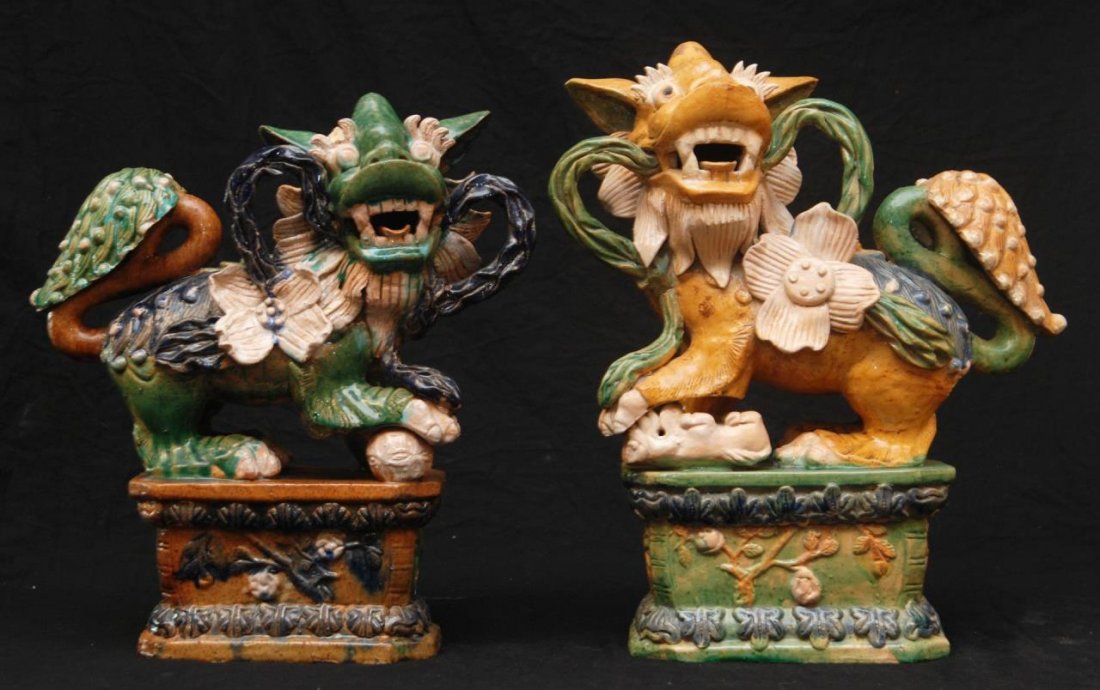 Pr OF CHINESE SANCAI GLAZE POTTERY FOO LIONS: A pair of Chinese Sancai glaze pottery foo lions. Each holding flower on stalk to mouth. The male with ball under paw and female with cub. Impressed fan mark to bottoms. Circa Qing dynasty to Republic