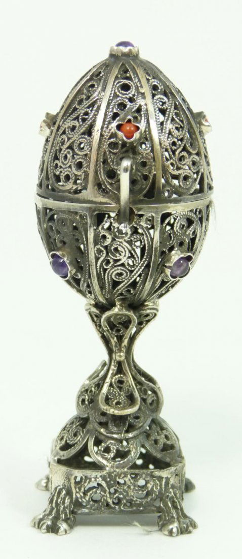 RUSSIAN SILVER JUDAIC FILIGREE SCENT BOX: A Russian filigree silver egg form scent box having a scrolled design throughout. Jeweled with amethyst and red coral. Seated Hasid surprise inside egg. Holds 84 silver purity mark with town, maker an