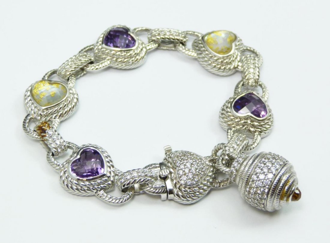 JUDITH RIPKA STERLING SILVER CHARM BRACELET: Judith Ripka sterling silver charm bracelet holding numerous round pave set white cubic zirconia stones. Heart shaped purple and white with gold flecking stones set to heart shaped links. Marked 'JUDI