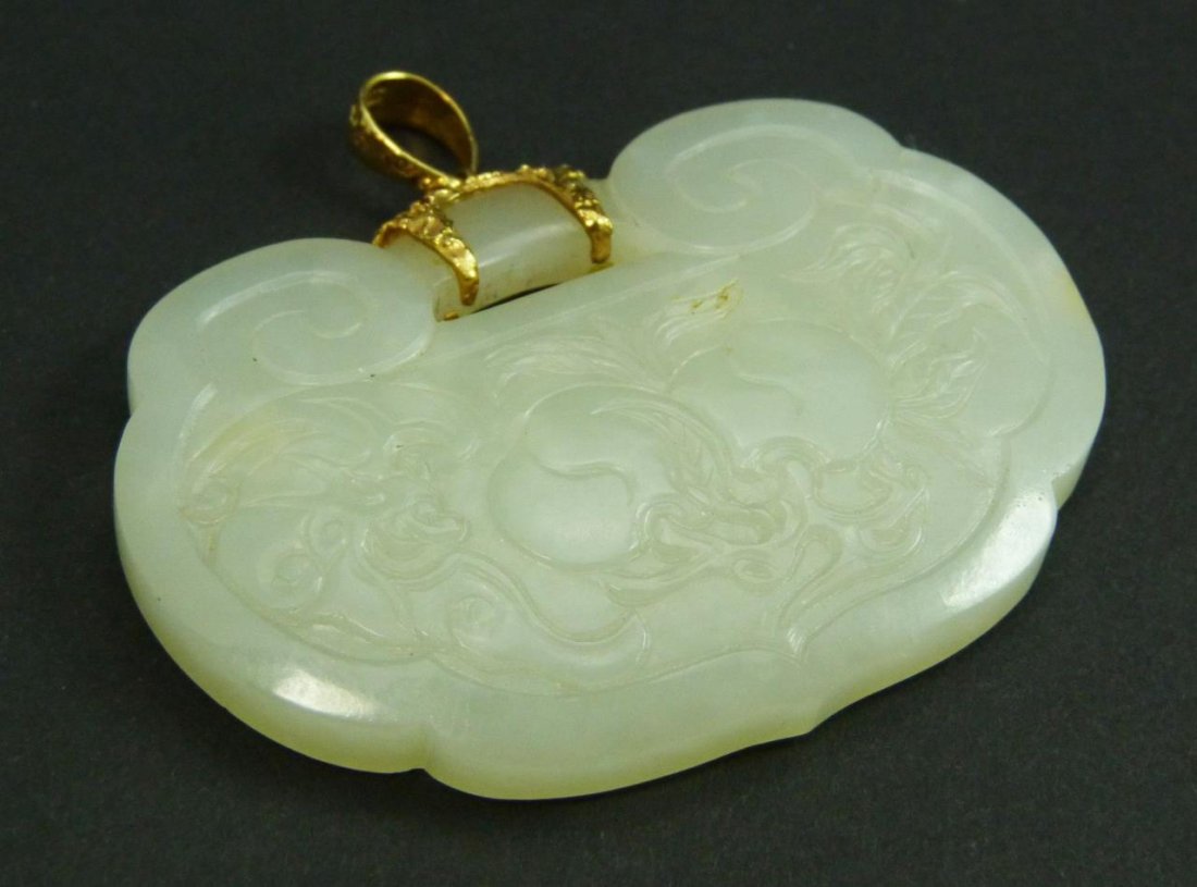 CHINESE 14K YG CARVED WHITE JADE LINZGHI PENDANT: A 20th century Chinese carved white jade figural lingzhi pendant having a 14K yellow gold bail. Pendant carved in relief depicting peaches and bats to front and a sea scene with dragon fish and pagoda
