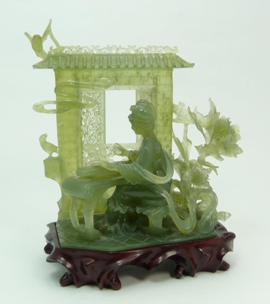 CHINESE CARVED SERPENTINE JADE GROUP: A nicely carved Chinese translucent green serpentine jade sculpture depicting a meiren playing a zheng. Behind her is wall with moving reticulated windows. Surrounded by foliage and flying birds. Incl