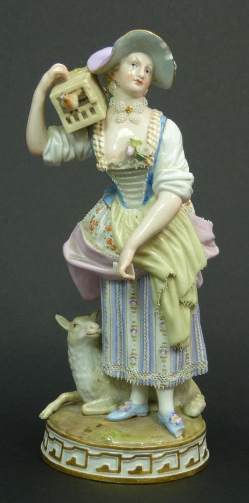 ANTIQUE MEISSEN FIGURE OF WOMAN w BIRD CAGE: An antique Meissen German porcelain sculpture depicting a woman holding a bird cage over her right shoulder. A recumbent lamp can be seen at her feet. Round base with gold accenting. Bottom holds blue