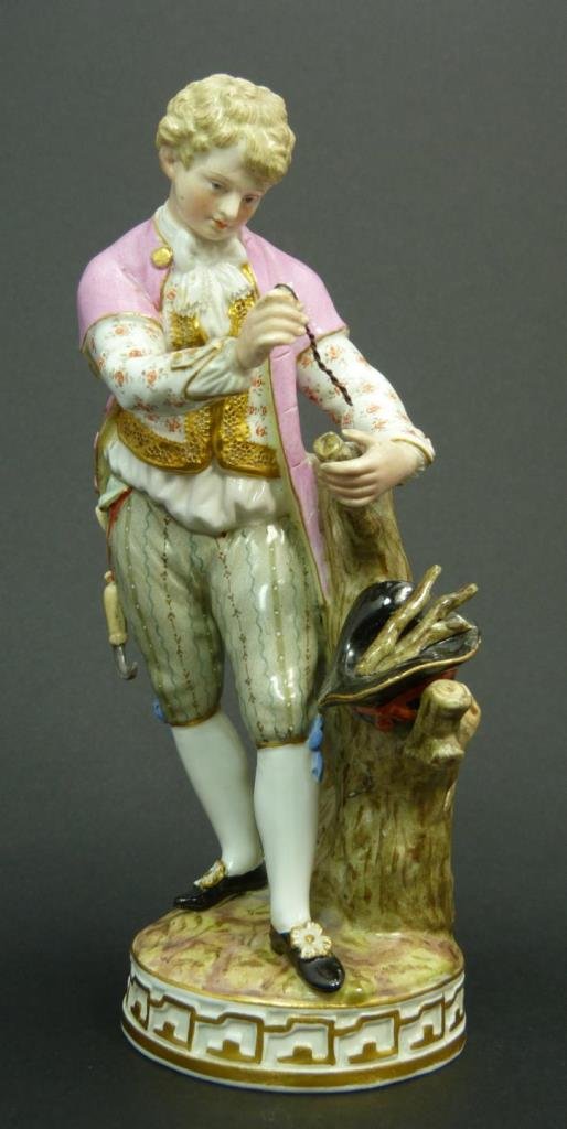 ANTIQUE MEISSEN FIGURE OF BOY CUTTING WOOD: A Meissen hand painted German porcelain sculpture depicting a standing young man cutting sticks from a branch. Round base with gold accenting. Bottom holds blue crossed swords marks. Etched 'F.69' and