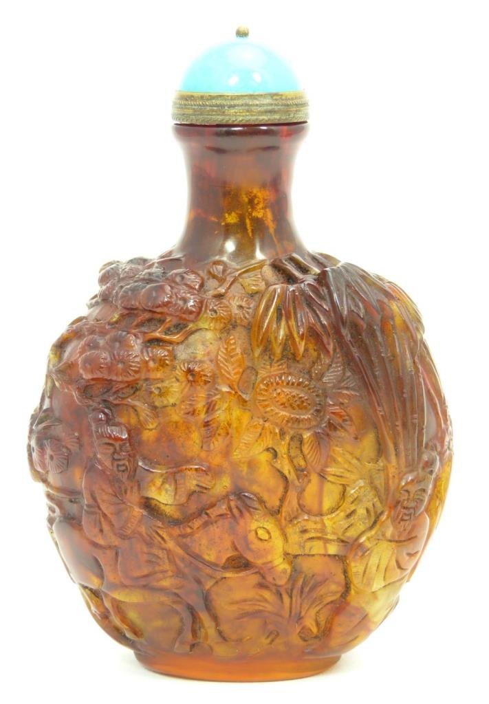 CHINESE HEAVY RELIEF CARVED AMBER SNUFF BOTTLE: A large and heavily relief carved Chinese amber snuff bottle. Depicts wisemen and attendant observing goats in a pine forest scene. Blue mottled stone stopper. Bottom holding etched Qing dynasty reign
