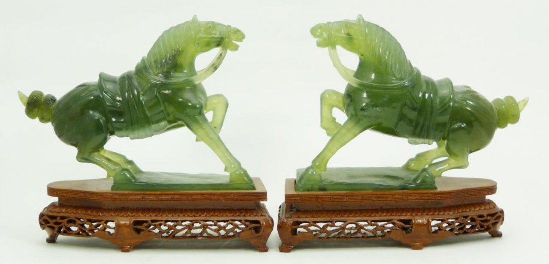 Pr CHINESE CARVED GREEN JADE HORSE FIGURES: A pair of Chinese carved green nephrite jade Tang horse sculptures. Each with imperial tack hoof up. Translucent pale green with spinach mottling. Circa 20th century. Includes fitted wooden bases. Mea