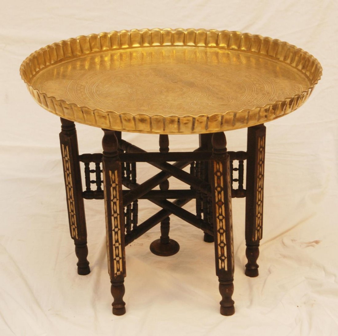 INDO-PERSIAN BRASS TRAY TABLE ON WOOD BASE: INDO-PERSIAN BRASS TRAY TABLE ON WOOD BASE This is a classic middle eastern table, used in tents by the Bedouin for centuries. It consists of a tooled copper tray set on folding wood legs. As in ages 