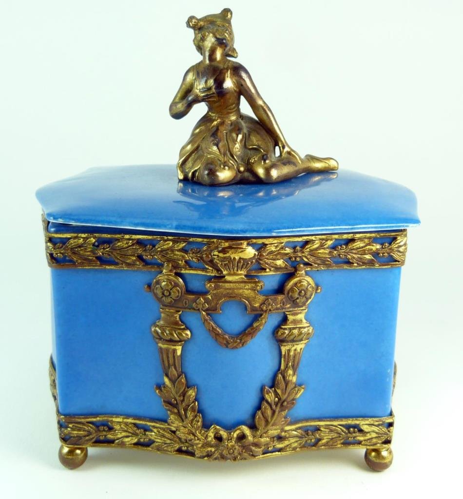 ANTIQUE GERMAN DECO PORCELAIN & BRONZE DRESSER BOX: Antique German deco porcelain and bronze dresser box depicting swooning as finial to top. Fleur-de-lis bronze mounts. Marked Germany. Measures 5" (12.7cm) Length x 6" (15.24cm) Height top to finial. T