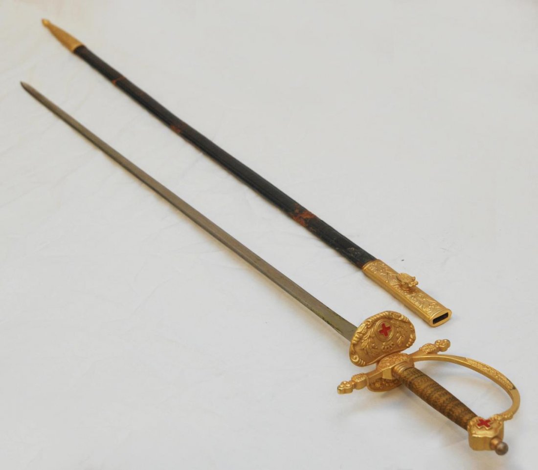 PERSONAL SWORD OF KING ALFONSO XIII: Original Toledo gold tone sword with red crosses of the King Alfonso XIII passed down and worn by Count Adrian Toati de Suiza de Bourbon. Comes with original leather sheath. Bears the royal crown on t
