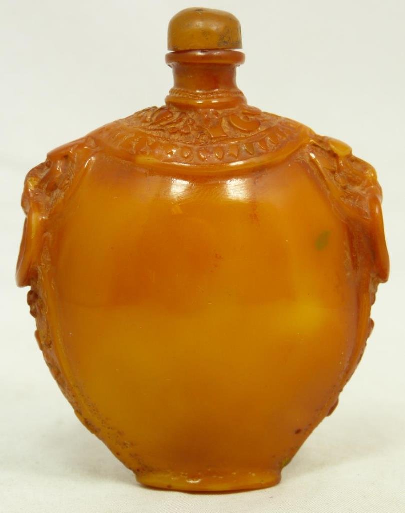 CHINESE CARVED GOLDEN AMBER SNUFF BOTTLE: Chinese carved golden amber snuff bottle having figural foo lions with rings handles to shoulders. Measures approx. 3 1/4" height x 2 5/8" width (8.3cm x 6.7cm). Total weight approx. 86 grams.
