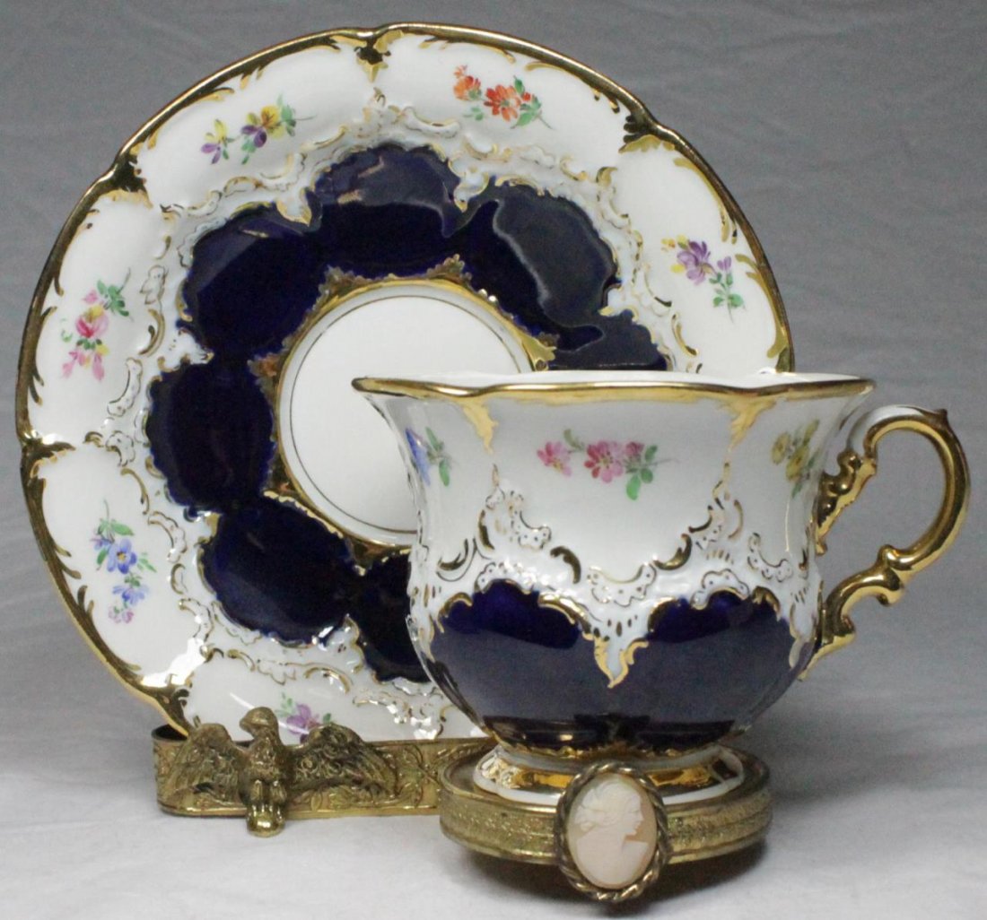 MEISSEN COBALT & GILT PORCELAIN TEACUP & SAUCER: Meissen porcelain cobalt and gilt porcelain teacup and saucer set with hand painted floral sprays. Factory 1st quality. Includes Ardalt Italian gilt metal display holder. Cup measures approx. 3" heigh