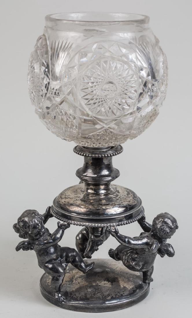Cut Glass Centerpiece Bowl and Stand: Globular cut glass vase in a silver plated figural stand with three putti. Height 16 1/4 inches. Notice to bidders: Condition reports and additional photographs are provided by request as a courtesy t