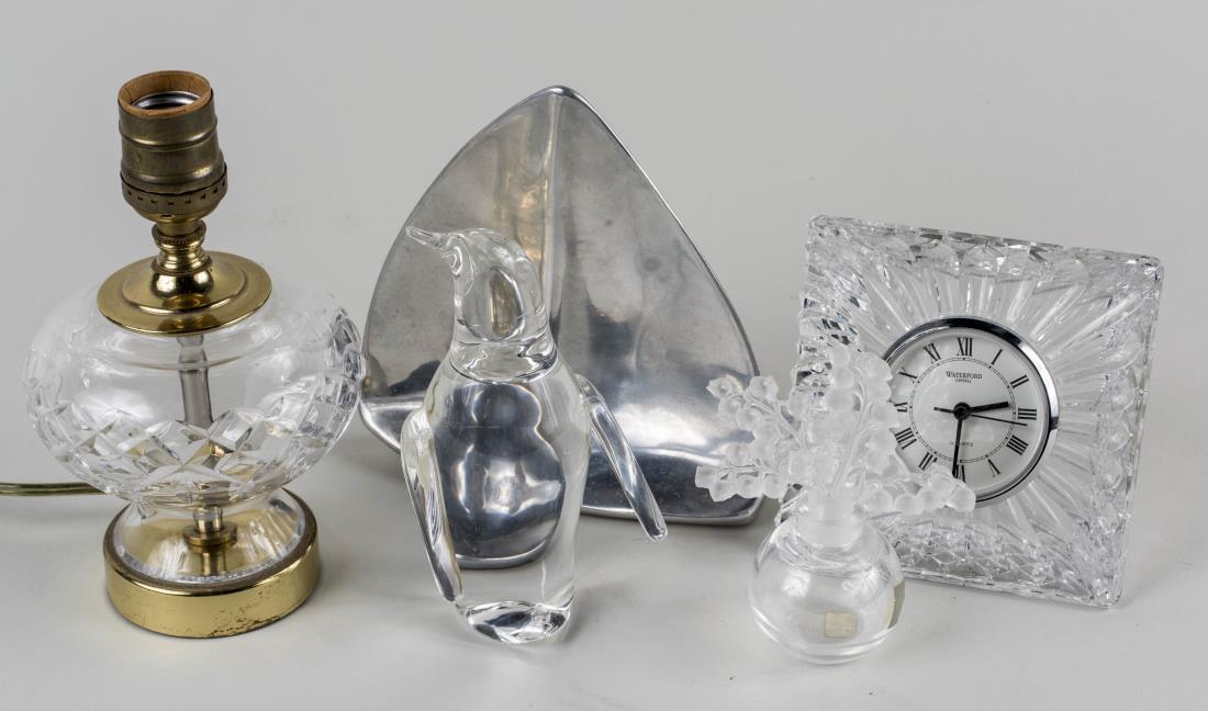 Group of Four Glass Decorations: Including a Lalique perfume bottle, a Stuben penguin, a Waterford desk clock, and a cut crystal boudior lamp, together with an aluminum sculpture of a sailboat. Lamp, height 7 3/4 inches. Notice to bi