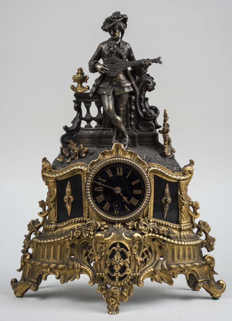 French Brass Figural Clock: Rococo style brass and patinated metal clock, dial with Roman numerals. Height 17 inches. Notice to bidders: Condition reports and additional photographs are provided by request as a courtesy to our c