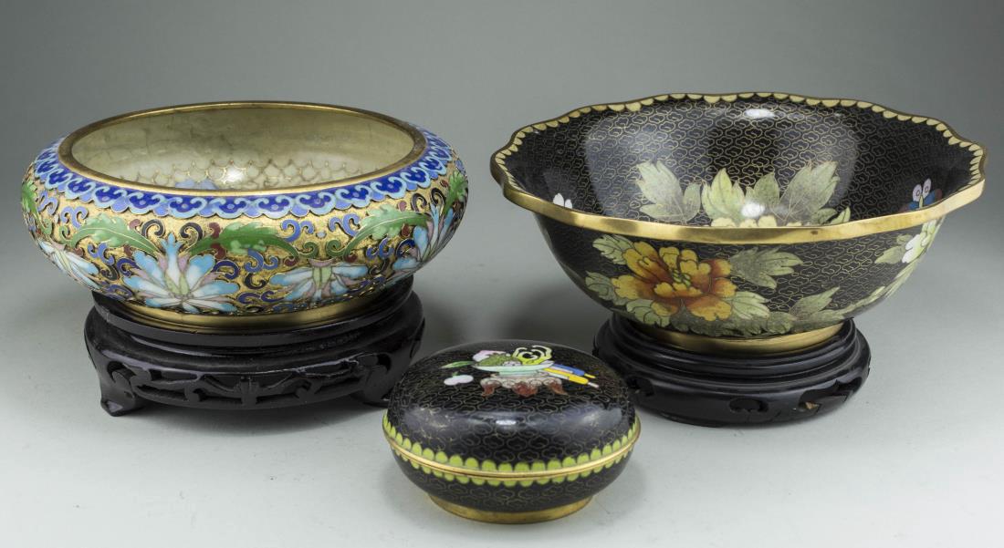 Three Chinese Cloisonne Table Articles: Comprising two bowls on carved wood stands, one with floral and butterfly decoration, the other with floral and scroll decoration, and a covered box with bowl of fruit decoration. Larger bowl height 2