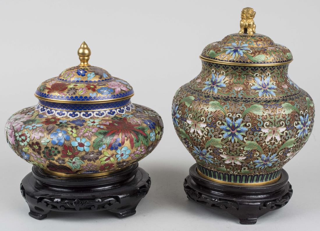 Two Chinese Cloisonne Covered Jars: One with foo lion finial, scroll and floral decoration, the other with turned finial and floral decoration, each on carved wood stand. Taller overall height 10 1/4 inches. Notice to bidders: Condition