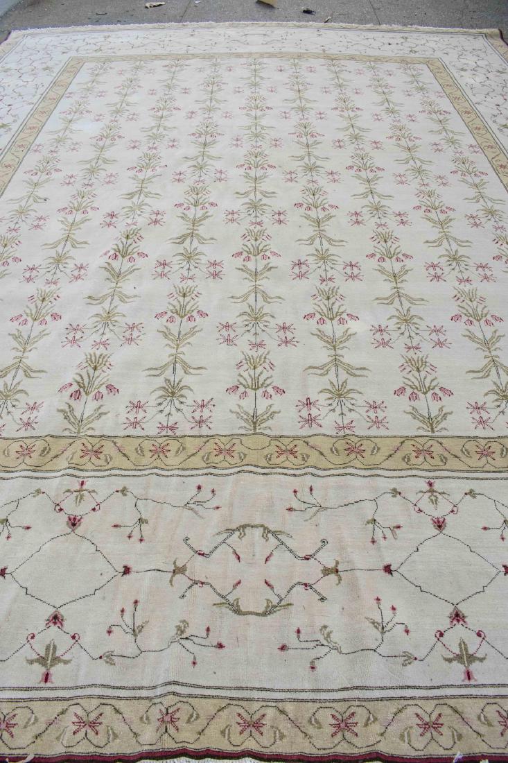 Romanian Agra-Style Carpet: Repeating geometric floral pattern on an ivory field, within a wide tan and ivory border with similar floral decoration. 15 feet 5 inches x 12 feet. Notice to bidders: Condition reports and additional