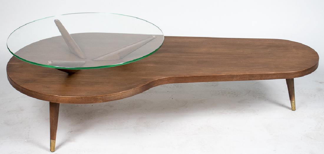 Vladimir Kagan Style Coffee Table: Circular glass shelf on three tapered supports above an asymmetric roughly kidney shaped wood top, on round tapered legs ending in brass sabots. Height 17 inches, width 54 inches, depth 27 inches. Not