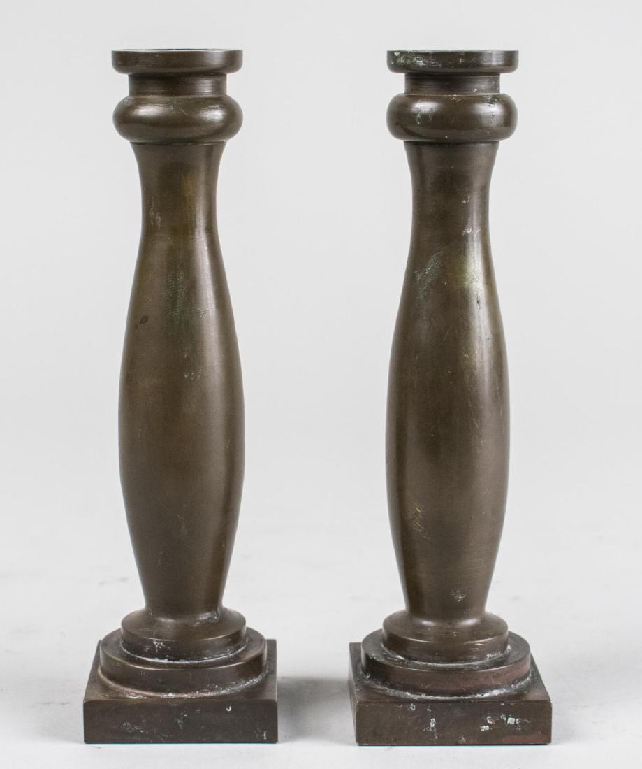 Pair of Tiffany Studios Bronze Candlesticks: Each an elongated baluster form candlestick on a square base, signed. Height 7 3/4 inches. Notice to bidders: Condition reports and additional photographs are provided by request as a courtesy to our 