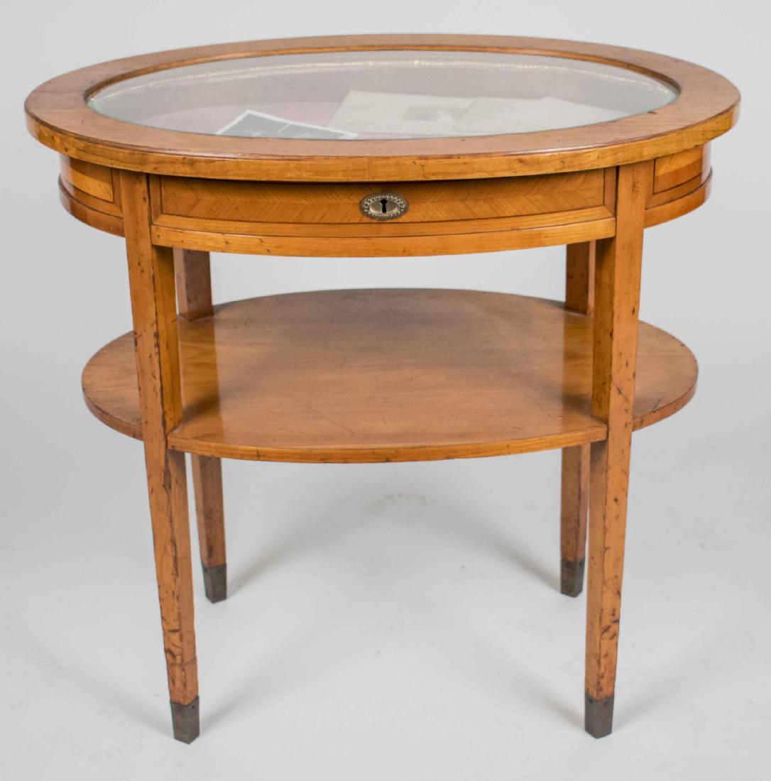 Vitrine Table: Oval glass inset lift top opening to a lined interior, on tapered square legs joined by a conforming lower shelf. Height 29 inches, width 30 inches, depth 20 inches. Notice to bidders: Condition repor