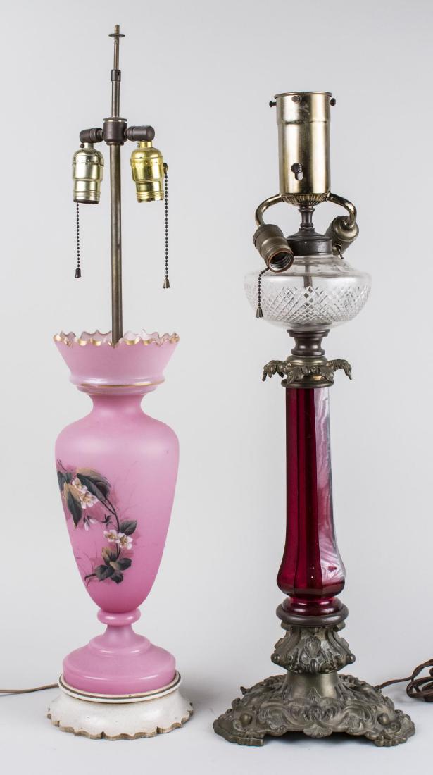 Two Glass Lamps: One a two light pink glass lamps with floral decoration, the other a metal mounted red glass converted oil lamp. Pink glass lamp base, height .18 1/2 inches. Notice to bidders: Condition reports and a