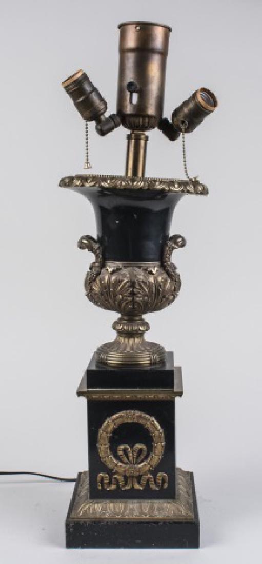 Urn Form Table Lamp: Two light lamp, black painted lamp with gilt brass neoclassical style decoration. Height, base, 18 1/4 inches. Notice to bidders: Condition reports and additional photographs are provided by request a