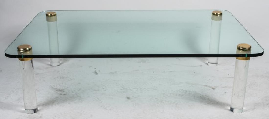 Lucite Glass Top Coffee Table: Rectangular top with rounded corners, on four round Lucite legs with brass accents. Height 16 inches, width 56 inches, depth 36 inches. Notice to bidders: Condition reports and additional photographs