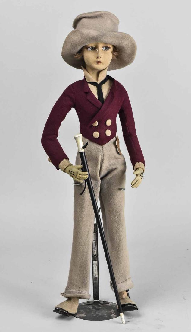 Lenci Doll: Felt doll with painted face, wearing a maroon jacket, beige pants and black leather and beige felt boots and a beige felt hat, with a walking stick, Lenci paper label. Height 24 inches. Notice to bidd