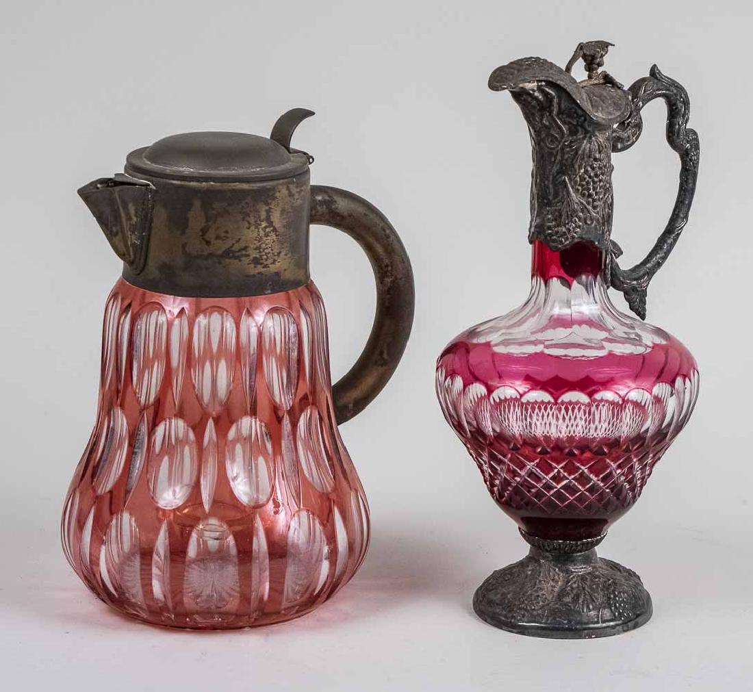 Two Metal Mounted Cut Glass Table Articles: Each cranberry cut to clear glass, one a silver plate mounted ewer, the other a metal mounted lemonade pitcher. Taller, height 12 1/2 inches. Notice to bidders: Condition reports and additional photog