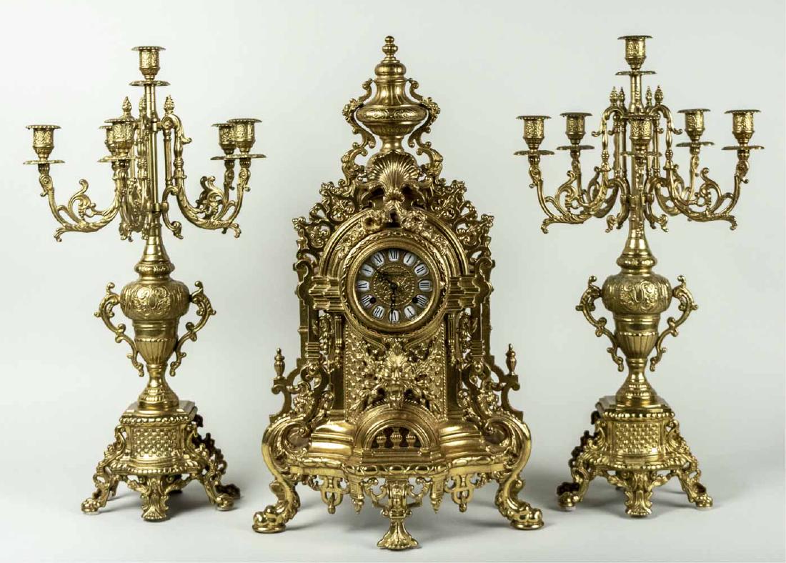 Brass Clock Garniture *: Rococo style with scroll decoration. Clock, height 24 inches. Notice to bidders: Condition reports and additional photographs are provided by request as a courtesy to our clients, as such any conditio