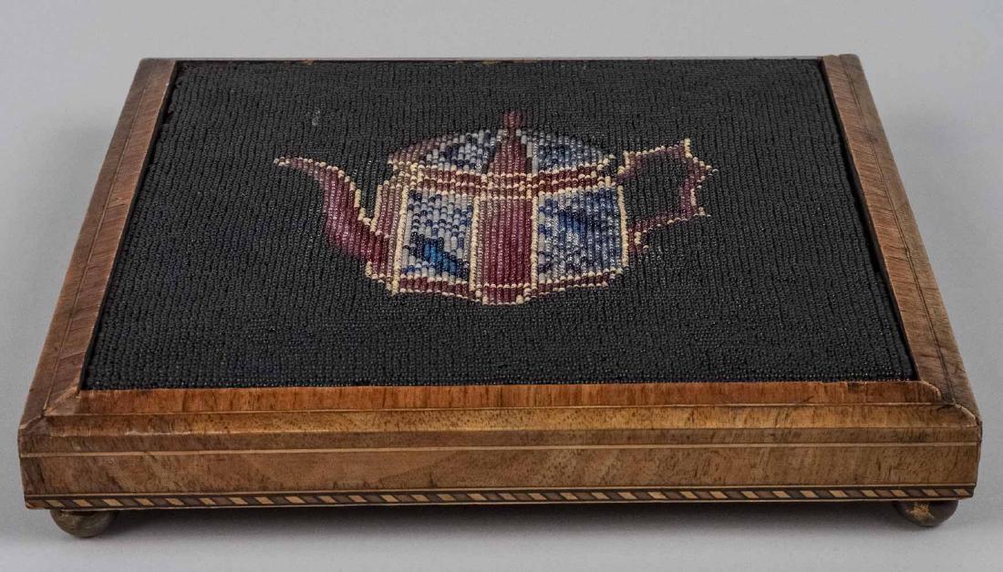 Victorian Bead Work Trivet: Decorated with a teapot. Height 2 inches, 10 1/2 inches square. Notice to bidders: Condition reports and additional photographs are provided by request as a courtesy to our clients, as such any condit