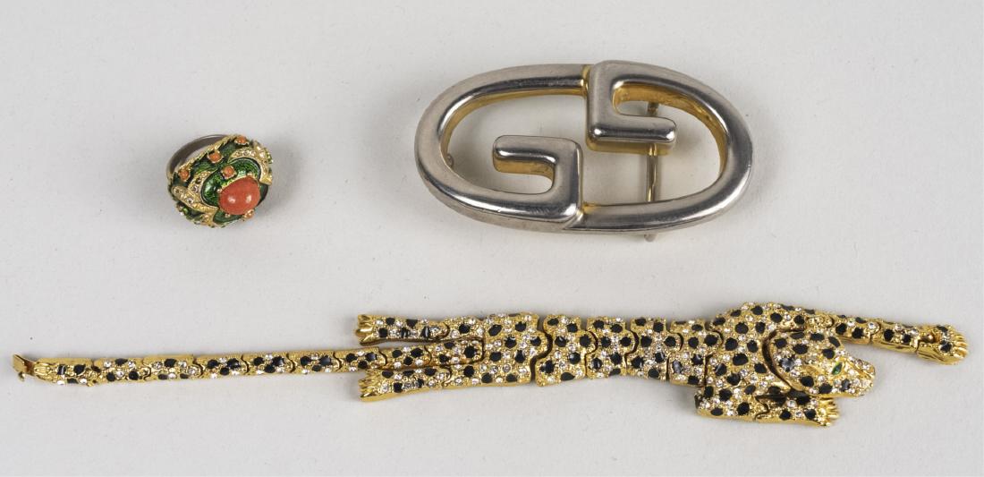 Three Designer Jewelry Articles: Comprising a Marvella ring, size 6, s Gucci belt buckle and a Cartier style articulated Panther Panther pin. Pin, length 8 inches. Notice to bidders: Condition reports and additional photographs are p