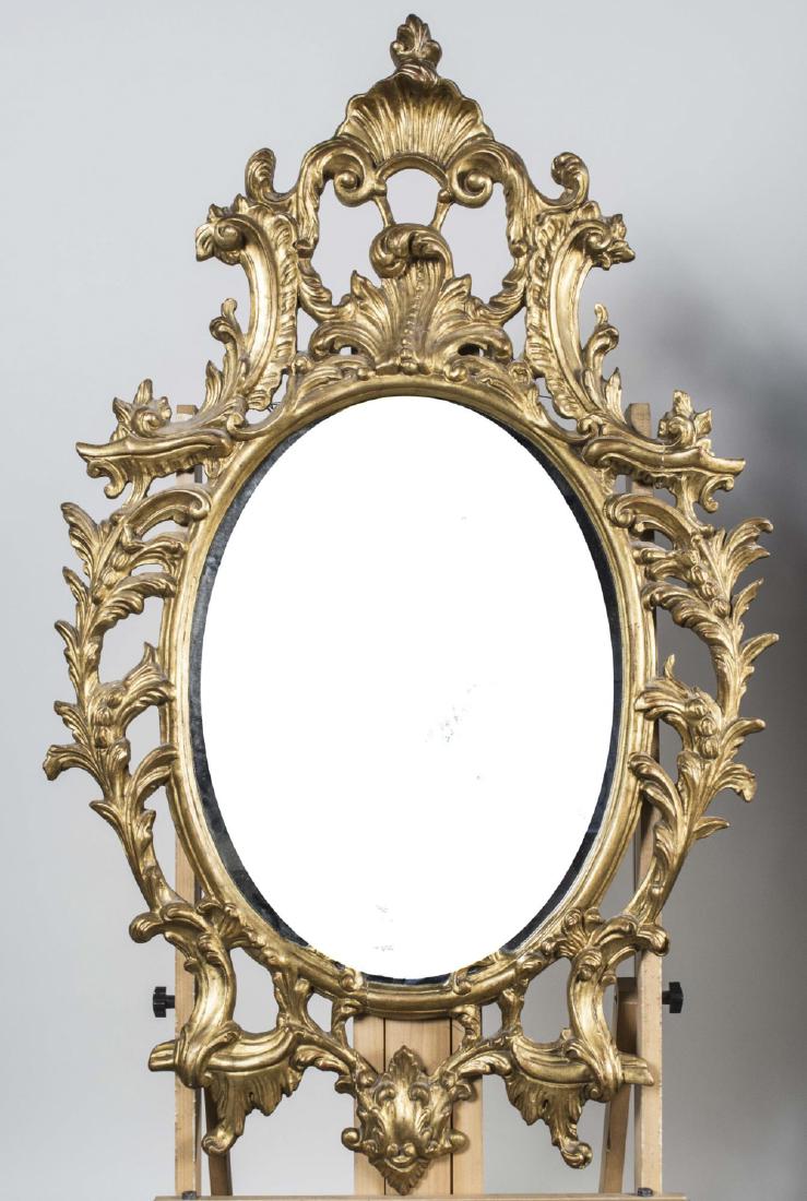 Rococo Style Gilt Wood Mirror: Oval mirror plate, the frame with scroll, foliate and shell decoration. Height 50 inches, width 32 inches. Notice to bidders: Condition reports and additional photographs are provided by request as a 