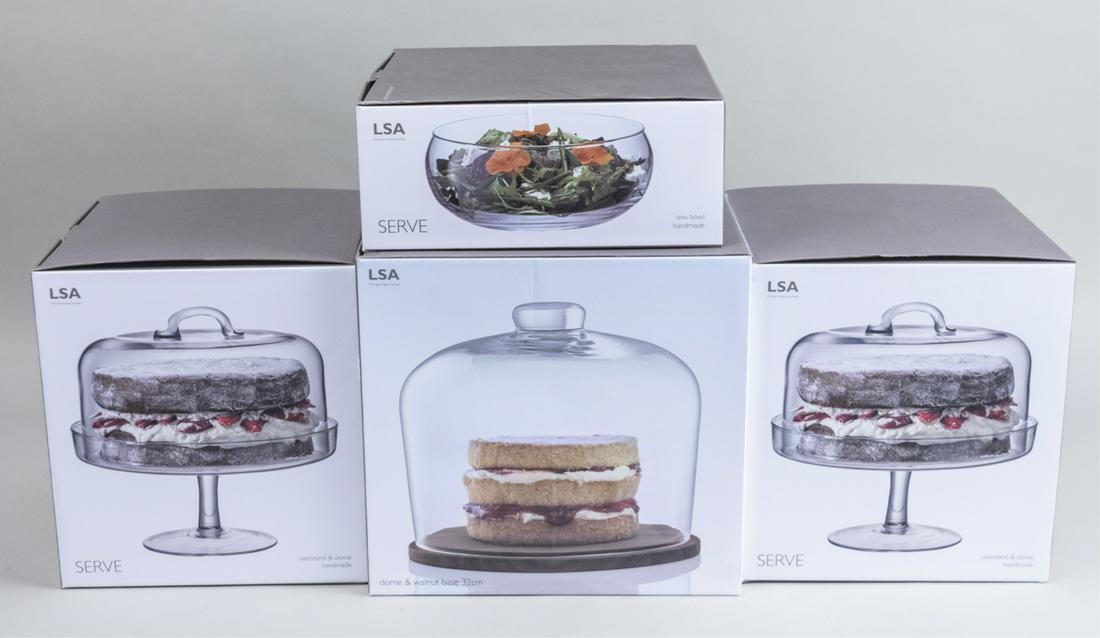 Four LSA International Glass Serving Dishes: Including two cake stands, a dome with oak base, and a salad bowl, in original boxes. Notice to bidders: Condition reports and additional photographs are provided by request as a courtesy to our clien