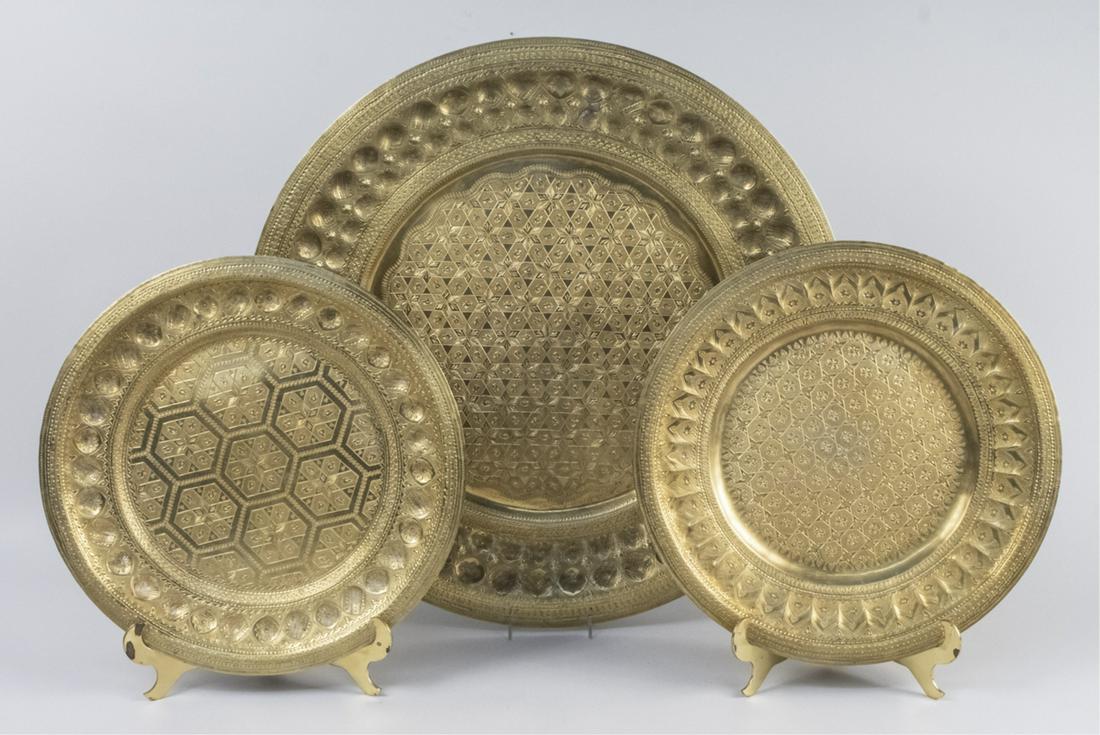 Three Brass Circular Trays: All hand hammered with intricate geometric, multi-dimensional designs. May be used on an ottoman or a top for small table. Signed in Arabic, diameter 23 ¾ inches and a smaller pair with brass display