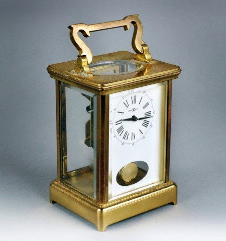 Howard Miller Carriage Clock: Brass case, white dial with Roman numerals, time and striking on a bell. Height over handle 7 1/4 inches.