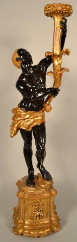Carved Wood Blackamoor Torchiere: Parcel gilt and part ebonized standing figure of a blackamoor holding a floral decorated torch. Height 65 inches.
