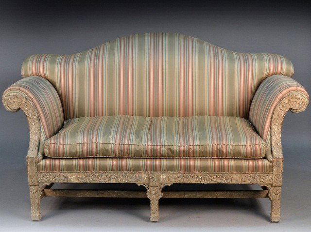 George III Style Upholstered Limed Wood Settee *: Camel back, flanked by outscrolled arms, cushion seat, floral carved square legs. Height 43 inches, length 6 feet, depth 36 inches.