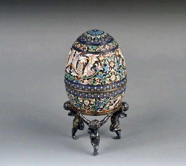 Russian Silver Egg on Stand *: Varicolored enamel decorated silver egg, height 5 inches, together with a Russian silver figural stand, height overall egg with stand 7 1/2 inches.