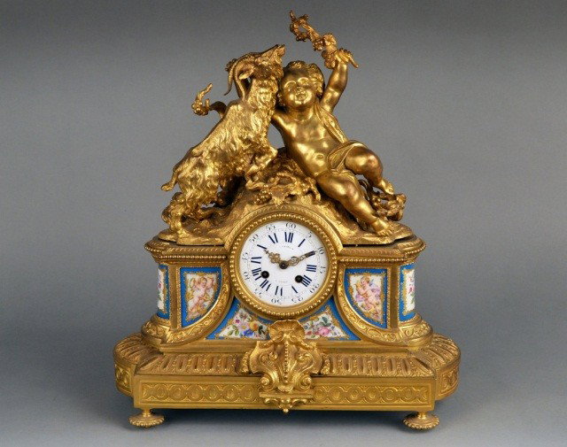 Louis XVI Gilt Bronze and Porcelain Clock *: By Antoine Crosnier, circa 1770, enamel dial with Roman numerals and Arabic seconds surmounted by a putto and a goat, the case inset with Sevres polychrome painted floral plaques. Height 18 inches.
