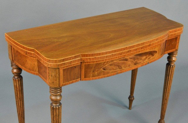 Sheraton Style Mahogany Card Table by Baker: Shaped rectangular top with slightly bowed front, opening on double swinging, tapered and reeded legs. Height 29 1/2 inches, width 36 inches, depth 17 inches.