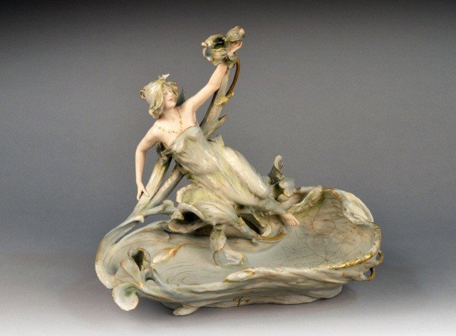 Royal Dux Porcelain Centerpiece: Modelled as a young woman holding an iris, the bowl decorated with a gilt spider web. Height 18 inches.