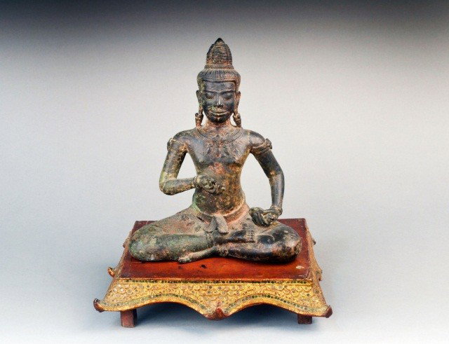 Cambodian Gilt Bronze Buddha: Modeled seated on a red painted parcel gilt carved wood stand. Height 11 1/4 inches.