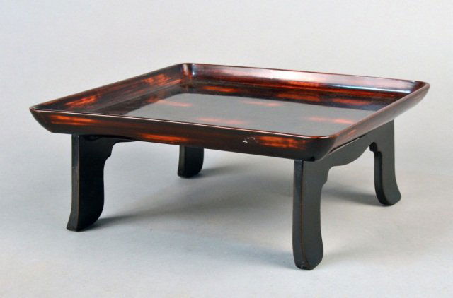Japanese Black and Red Lacquered Tray: Shaped square form on four legs. Height 6 inches, width 14 1/4 inches, depth 14 1/4 inches.