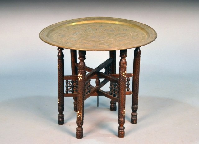 Middle Eastern Brass & Inlaid Wood Low Table: Brass circular top on a folding carved wood stand. Height 21 1/2 inches, diameter 24 1/2 inches.