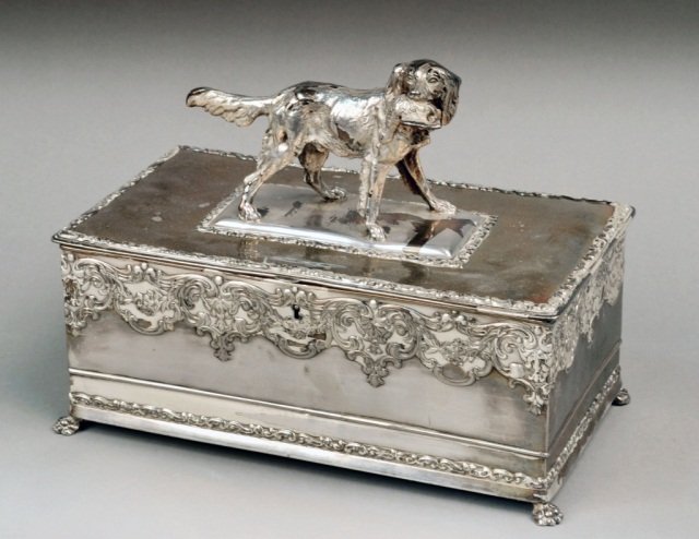 Meriden Silver Plated Casket: Rectangular, scroll decoration, the lid surmounted by a dog with bird in his mouth. Height 9 1/2 inches, width 12 inches, depth 7 inches.
