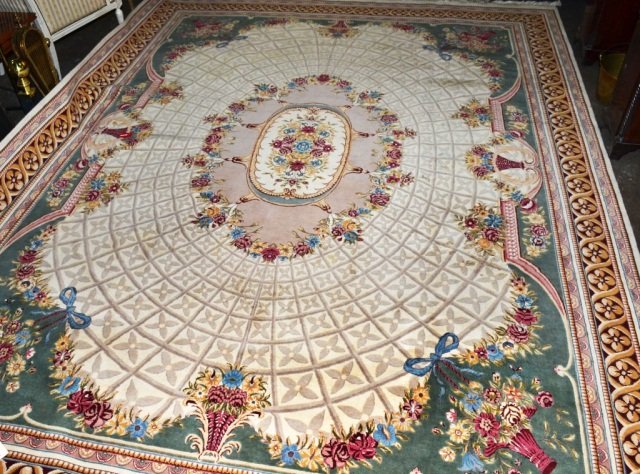 Aubusson Style Carpet: Central floral medallion on an ivory field with flower in basket decoration around the edge, all within a guard border with stylized floral and ribbon decoration. 12 feet 9 inches x 9 feet 3 inches.