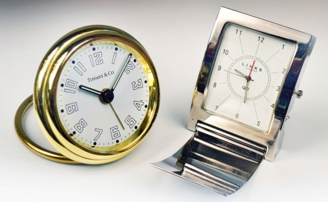 Tiffany Quartz Travel Clock: With white dial, illuminated hands, alarm function, gold tone finish, black leather case and blue tiffany bag, diameter 2 3/8 inches; together with Links of London travel clock,